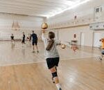 Coed volleyball team practicing indoors, focusing on teamwork and skill development.