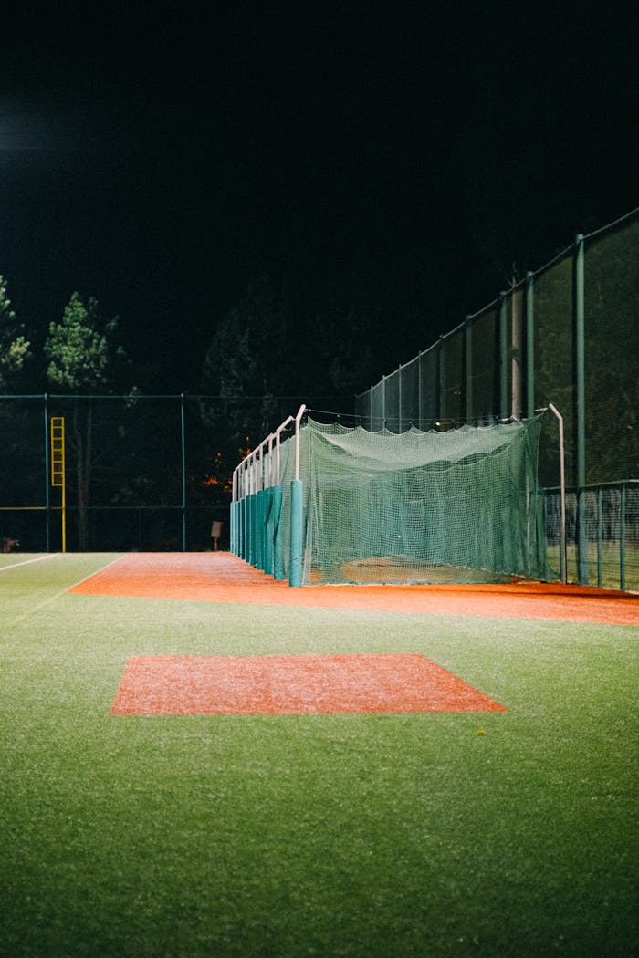 A brightly lit sports field at night featuring netting and lush green grass, ideal for concept sports imagery.