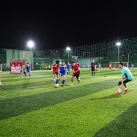 Young athletes playing a competitive soccer match on a lit artificial turf field at night.